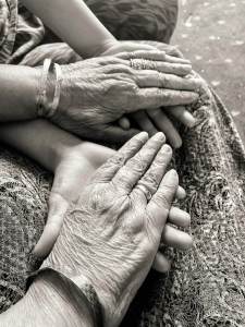 A loving black-and-white photograph of wrinkled hands clasping young ones.